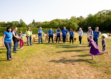 Personen verschiedener Altersgruppen stehen und bilden einen Halbkreis auf einer grünen Wiese.