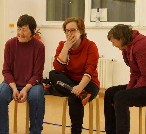 Drei Damen lachen, während sie nebeneinander auf Hockern sitzen.