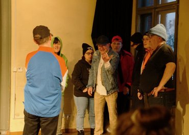 Sieben Personen stehen in einer Gruppe zusammen, eine weitere Person geht auf sie zu.