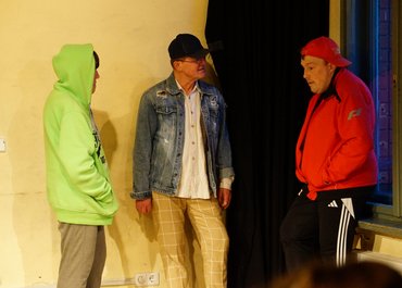Drei Personen stehen als Gruppe zusammen, alle tragen Jacken und Kappen.