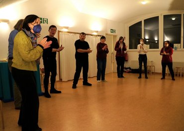 Personen stehen mit Abstand in einem Halbkreis und klatschen in die Hände.