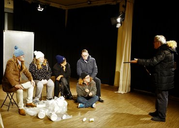 Eine Gruppe von fünf Personen werden von einem Mann angesprochen.