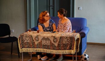 Zwei Damen sitzen auf einem Sofa und sprechen miteinander.