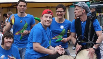Fünf Personen aus der Trommelgruppe spielen gemeinsam, eine Person lächelt in die Kamera.
