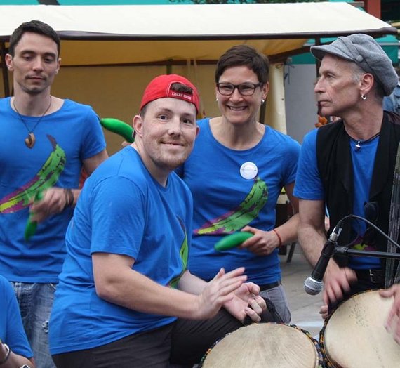 Fünf Personen aus der Trommelgruppe spielen gemeinsam, eine Person lächelt in die Kamera.