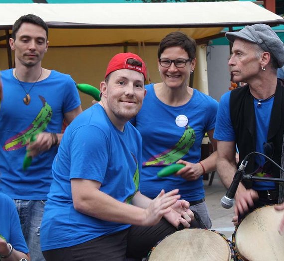 Fünf Personen aus der Trommelgruppe spielen gemeinsam, eine Person lächelt in die Kamera.