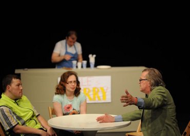 Drei Personen in einer hitzigen Unterhaltung an einem Esstisch.