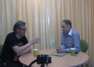 Zwei Männer sitzen an einem Tisch und sprechen miteinander.