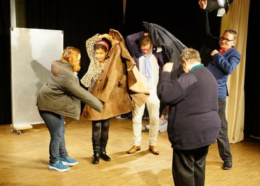 Fünf Darsteller ziehen sich Winterjacken an.